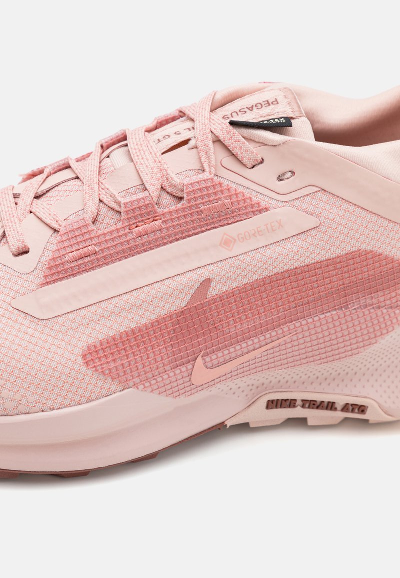 Zapatilla de color rosa claro con parte superior de malla texturizada, etiqueta GORE-TEX y un diseño estampado en el lateral, con suela de goma y suela para senderos.