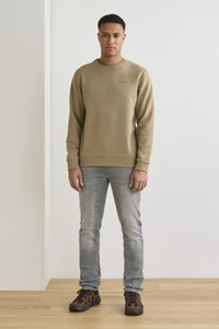 Sudadera marrón claro con puños y bajo acanalados, combinada con jeans azul claros y zapatillas marrones y negras. Diseño minimalista, sin patrones.