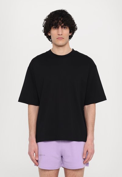 Camisa negra de gran tamaño con mangas cortas, cuello redondo y textura suave. Combinada con pantalones cortos de color púrpura claro con un diseño sencillo.