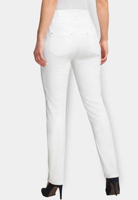 Witte denim jeans met een aansluitende taille en achterzakken, voorzien van een rechte pijpontwerp en subtiele stikdetails. Gedragen met hoge hakken.