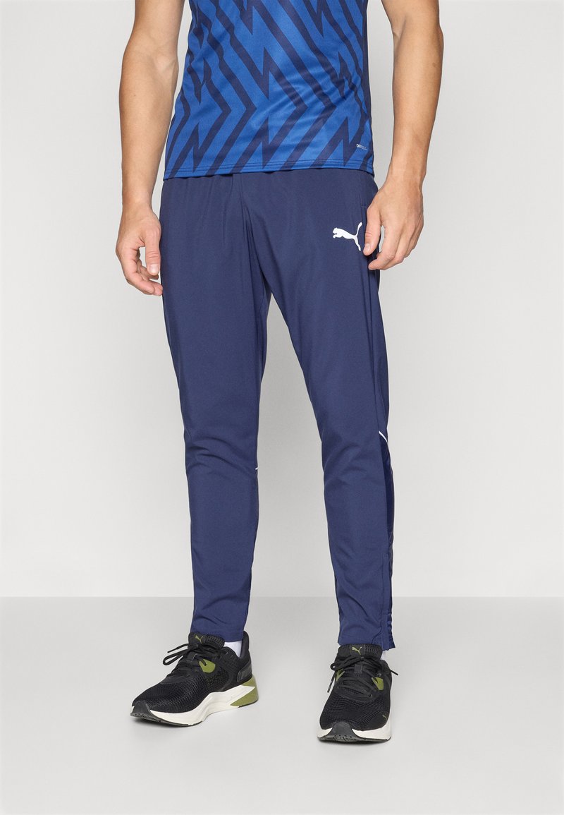 Pantalones deportivos en color navy, fabricados con un tejido ligero y de corte ajustado, con detalles en blanco en el logo y una textura suave, combinados con zapatillas negras.