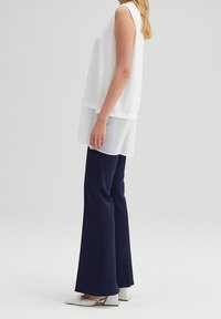 Wit mouwloos topje met een geplooide ondersectie, gecombineerd met marineblauwe flared pants en zilveren blokhak schoenen. Minimalistisch ontwerp.