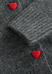 Grey knitted fabric with ribbed texture and two small red knitted heart shapes sewn onto it.