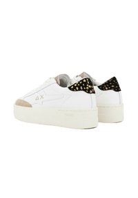 Witte sneakers met een gestructureerde beige neus, een zwarte en gouden gevlekte achterzijde en een dikke witte zool. Veters zijn door oogjes geregen.