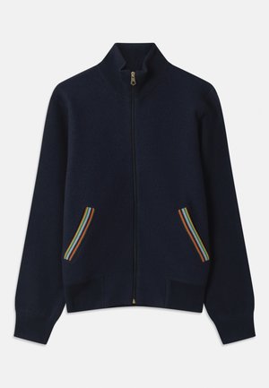 Tumši zils zip-up džemperis ar augstu apkakli, kas aprīkots ar divām kabatām, kas rotātas ar varavīksnes svītrām un zelta rāvējslēdzēju. Mīksta tekstūra, brīvs piegriezums.