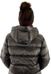 Giacca a vento nera con finitura lucida e cappuccio; presenta sezioni imbottite orizzontali. Berretto in maglia marrone con righe nere e pompon in pelliccia.