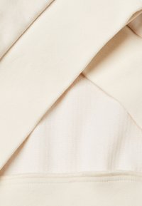 Capas de tejido color crema con diferentes texturas; una es suave mientras que la otra tiene un patrón acanalado. Las costuras están acabadas de manera ordenada.