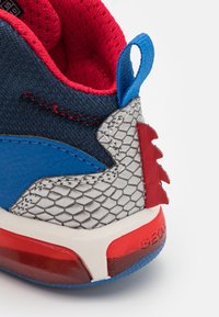 Sininen ja punainen lenkkari, jossa on harmaa teksturoitu kanta, jossa on hexagonaalinen kuvio, pehmustettu punainen sisus ja sininen vetotakki.