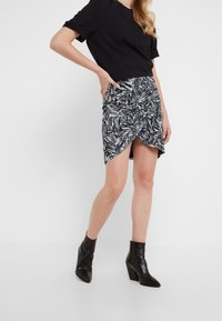 T-shirt nero abbinato a una mini gonna a vita alta con pattern floreale, caratterizzata da un design avvolgente e orlo asimmetrico, indossata con stivali neri alla caviglia.