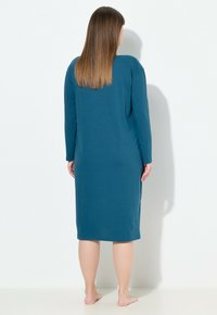 Vestido de manga larga en color azul verdoso, confeccionado en una tela suave, con un corte recto que llega por debajo de la rodilla, con un escote redondo y sin patrones visibles.