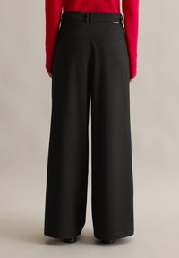 Pantalones de pierna ancha negros de talle alto con un acabado texturizado, que cuentan con dos bolsillos traseros y presillas para cinturón, mostrados desde la parte posterior.