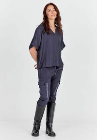 Námornícky modrý top s krátkym rukávom a výstrihom do V s textúrovanými pásikmi, v kombinácii s tmavými cargo nohavicami so zipsami a bočnými vreckami, nosený s čiernymi vysokými čižmami po kolená.