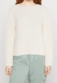 Suéter de punto acanalado crema con mangas largas, un escote redondo y un corte recto, combinado con pantalones cargo verde claro.