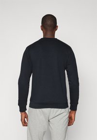 Zwarte lange mouw sweatshirt met een ronde halslijn, geribde mouwen en zoom. Zacht materiaal, minimalistisch ontwerp, gedragen over grijze joggingbroeken.