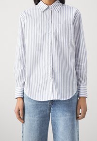 Košile na knoflíky z lehké látky s modrými a bílými vertikálními pruhy, náprsní kapsou a dlouhými rukávy s manžetou.