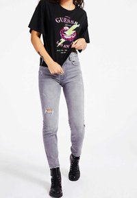 Camiseta gráfica negra con estampado en rosa y verde, combinada con jeans skinny desgastados en gris y botas negras con cordones.