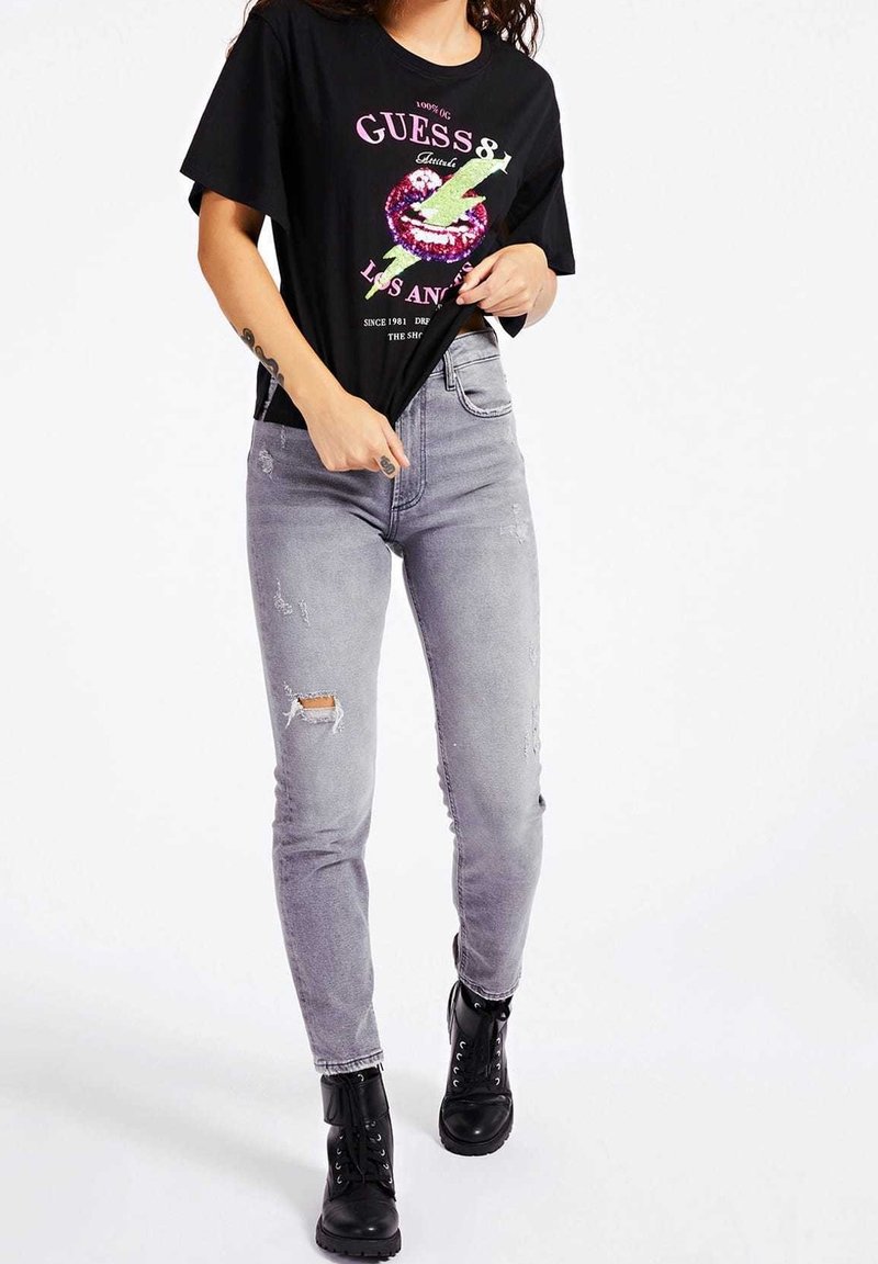 Camiseta gráfica negra con estampado en rosa y verde, combinada con jeans skinny desgastados en gris y botas negras con cordones.