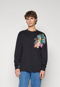 Maglietta nera a maniche lunghe con grafiche colorate sul lato sinistro del petto, tra cui volti e simboli, realizzata in tessuto di cotone.