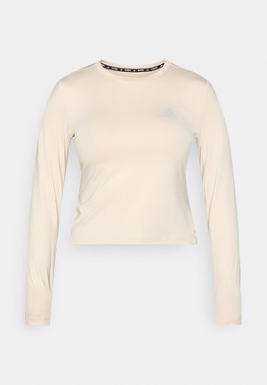 Lys beige langermet atletisk topp med cropped design, glatt tekstur og en liten blå Adidas-logo på brystet. Markert krage.