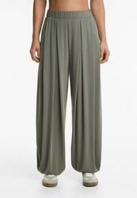 Pantaloni larghi di un verde chiaro con vita elastica arricciata, realizzati in un tessuto morbido, caratterizzati da pieghe verticali e un design fluido.