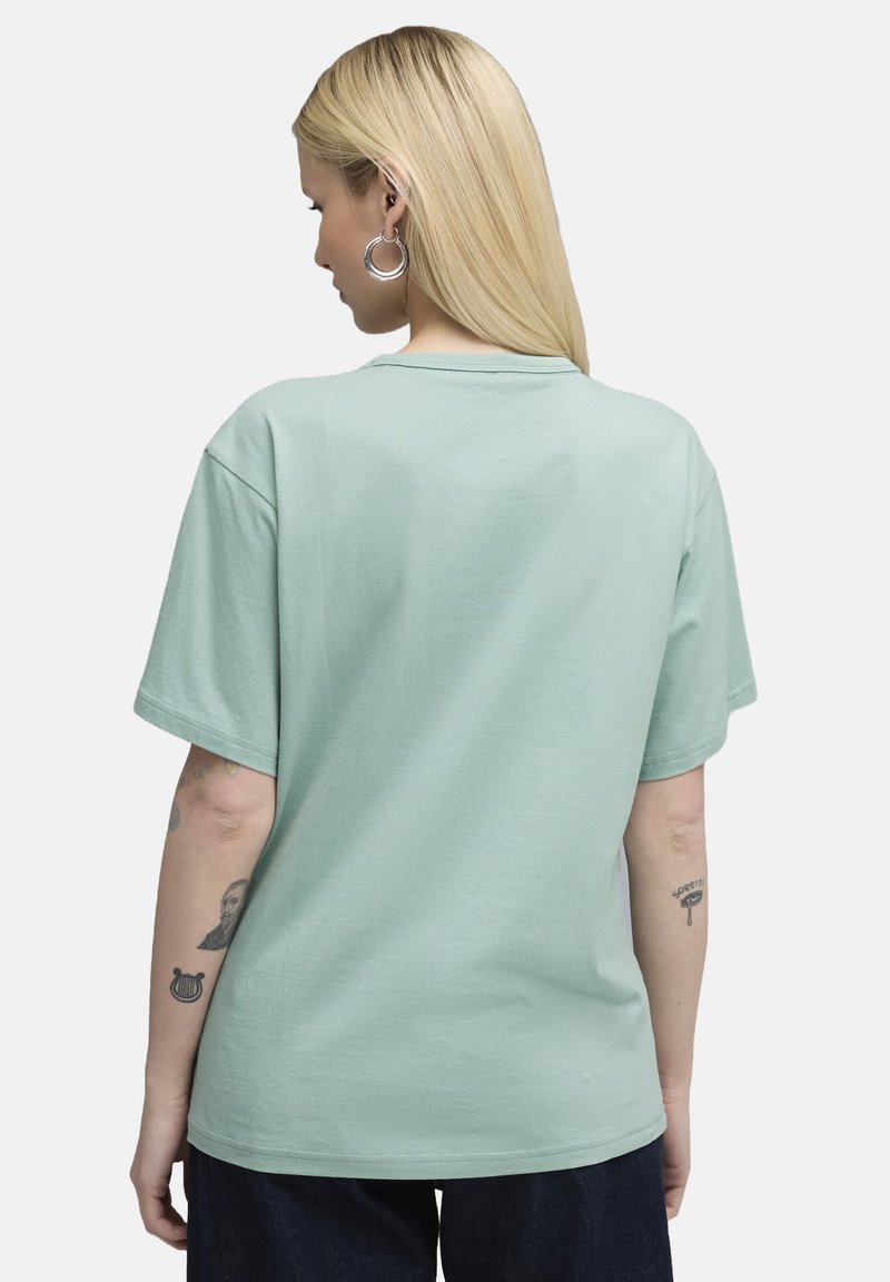 Miętowy bawełniany t-shirt z krótkim rękawem, okrągłym dekoltem i luźnym krojem. Widoczne tatuaże na ramieniu. Prosty widok z tyłu.