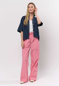 Oversized denim overhemd met korte mouwen, witte tanktop eronder, en roze wijde broek met fijne strepen en een aantrekkoord in de taille.