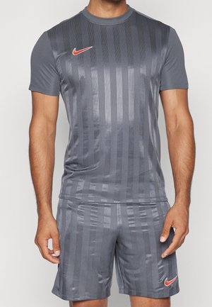 Mand iført mørkegrå stribet sportstrøje og matchende shorts med røde Nike-logoer på brystet og venstre lår.