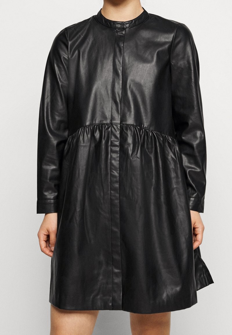 Svart läderklänning med rund krage, långa ärmar, en rynkad midja och rak passform. Har en knappstängning framtill.