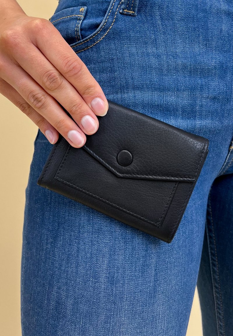 Black leather wallet with a textured finish, featuring a triangular flap closure and a snap button, held against blue denim jeans.