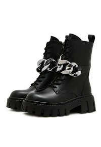Bottes chelsea noires à lacets avec semelle épaisse, cuir lisse, détail de chaîne argentée et fermeture éclair. Dotées d'une semelle crantée robuste et d'une languette de traction.