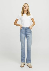 Svijetloplavi traperu flared traperice s visokim strukom, nosi se s bijelom prilagođenom majicom. Značajni detalji uključuju četiri džepa i minimalistički dizajn.