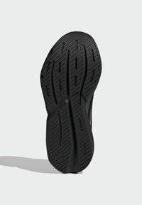 Čierna gumená podrážka topánky s diagonálnymi a vertikálnymi drážkami pre lepšiu priľnavosť, zobrazená na jednoduchom svetlosivom pozadí.