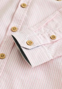Lyserød og hvid stribet skjorte med knapper lavet af træ, der har et kontrasterende mørkt manchetfor og blød tekstureret stof.