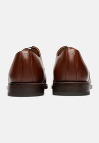 Scarpe in pelle marrone con finitura liscia, punta arrotondata, dettagli di cucitura minimi e suola in gomma marrone scuro. Design semplice, senza motivi.