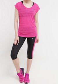Rosa träningsskjorta med ett subtilt randigt mönster, tillsammans med svarta capribyxor med en rosa sidostripe, samt rosa löparskor.