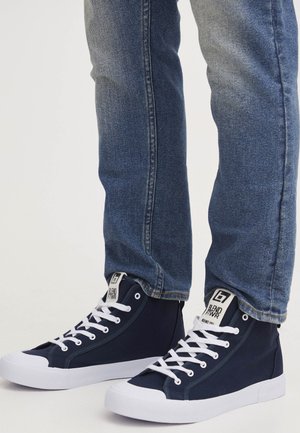 Zapatillas altas de marinero con suelas y cordones de goma blanca. Cuenta con una parte superior de lona, etiqueta con el logotipo en la lengüeta y costuras en contraste.
