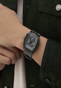 Montre chronographe à quartz avec un boîtier vert, un cadran gris et un bracelet en caoutchouc. Elle présente trois sous-cadrans et un design angulaire.