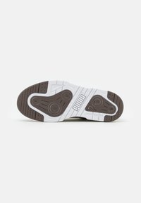 Pohja valkoisista ja tummanruskeista Puma-kengistä, joissa on teksturoitu pito-kuvio ja Puma-logo keskellä.