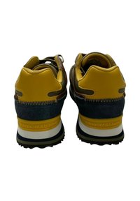 Sneaker con una tomaia sintetica gialla e dettagli marroni, con inserto in suede grigio sul tallone. Suola nera spessa con strisce bianche e gialle.