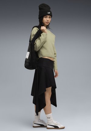 Sweatshirt court vert clair, jupe asymétrique noire, baskets blanches avec accents noirs, bonnet noir et sac fourre-tout en peluche noire.