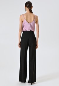 Camisola in satin rosa con spalline sottili, abbinata a pantaloni larghi neri a vita alta. Texture liscia e design semplice.