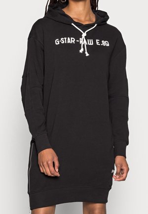 Black oversized hoodie dress with white drawstrings, G-Star Raw E.89 logo on chest, worn by person with braided hair.