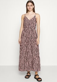 Maxikleid in Pink mit schwarzen Zickzackstreifen, dünnen Trägern, taillierter Taille und einem gestuften Rockdesign. Getragen mit schwarzen Sandalen.