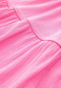 Texturiertes pinkes Gewebe mit einer zerknitterten Oberfläche, das weiche Falten und einen subtilen Glanz aufweist, was sein leichtes und luftiges Design hervorhebt.