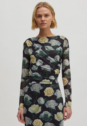 Langsleeve top in doorzichtig zwart materiaal met een bloemenpatroon van gele en witte rozen, met gerimpelde details langs de zijkanten.