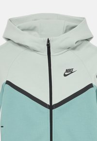 Nike hoodie σε απαλό μέντα με μαύρες λεπτομέρειες. Διαθέτει μπροστινό φερμουάρ, κουκούλα και γεωμετρικό color blocking στο στήθος.