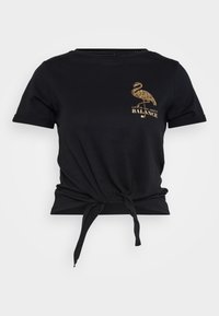 Svart T-skjorte med korte ermer og knyttet front, med et gullflamingo-grafikk og teksten "LIVET HANDLE OM BALANSE." Laget av bomull.