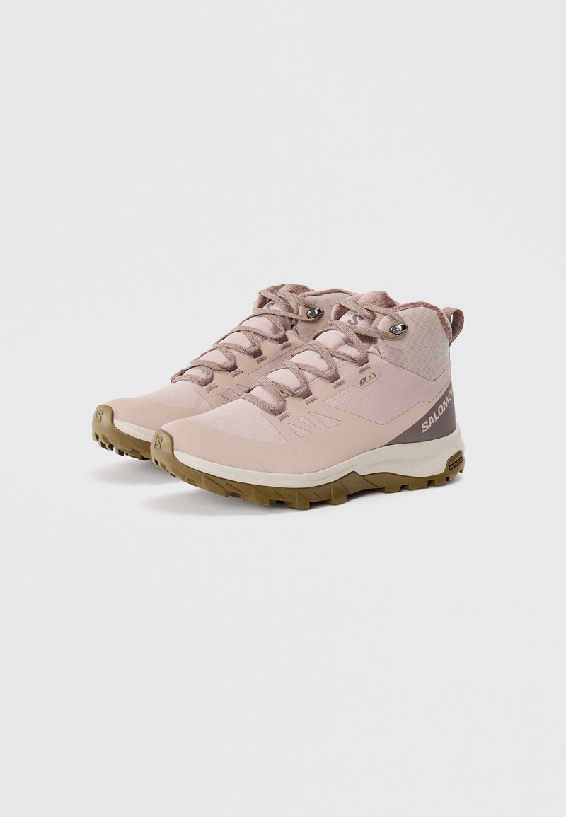 Bottes de randonnée rose clair avec un tissu texturé, des semelles robustes, des œillets ovales, et un accent de talon à motif dans une teinte plus foncée.
