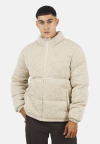 Giacca puffer beige con colletto alto, polsini a coste, chiusura con zip e tasche frontali. Tessuto testurizzato con un sottile motivo a Macchie.