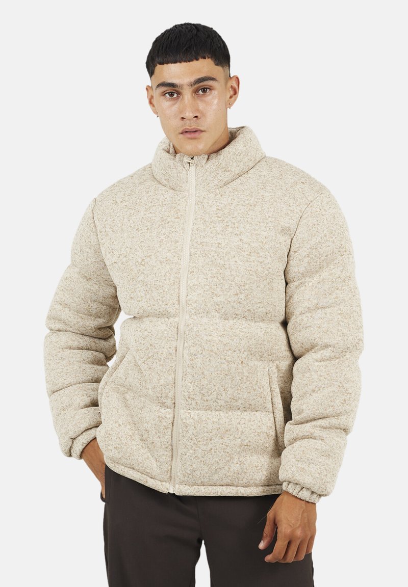 Giacca puffer beige con colletto alto, polsini a coste, chiusura con zip e tasche frontali. Tessuto testurizzato con un sottile motivo a Macchie.